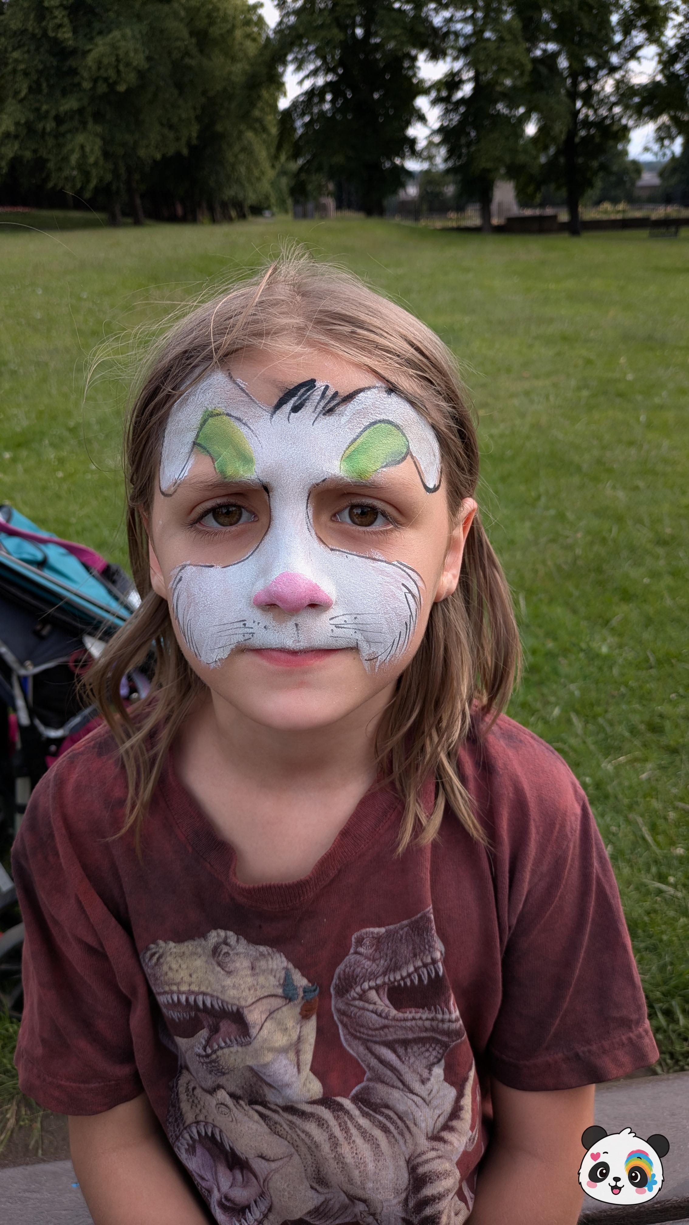 White bunny rabbit face paint with green inner ears, a pink nose, and black whisker details covering the forehead and nose area.