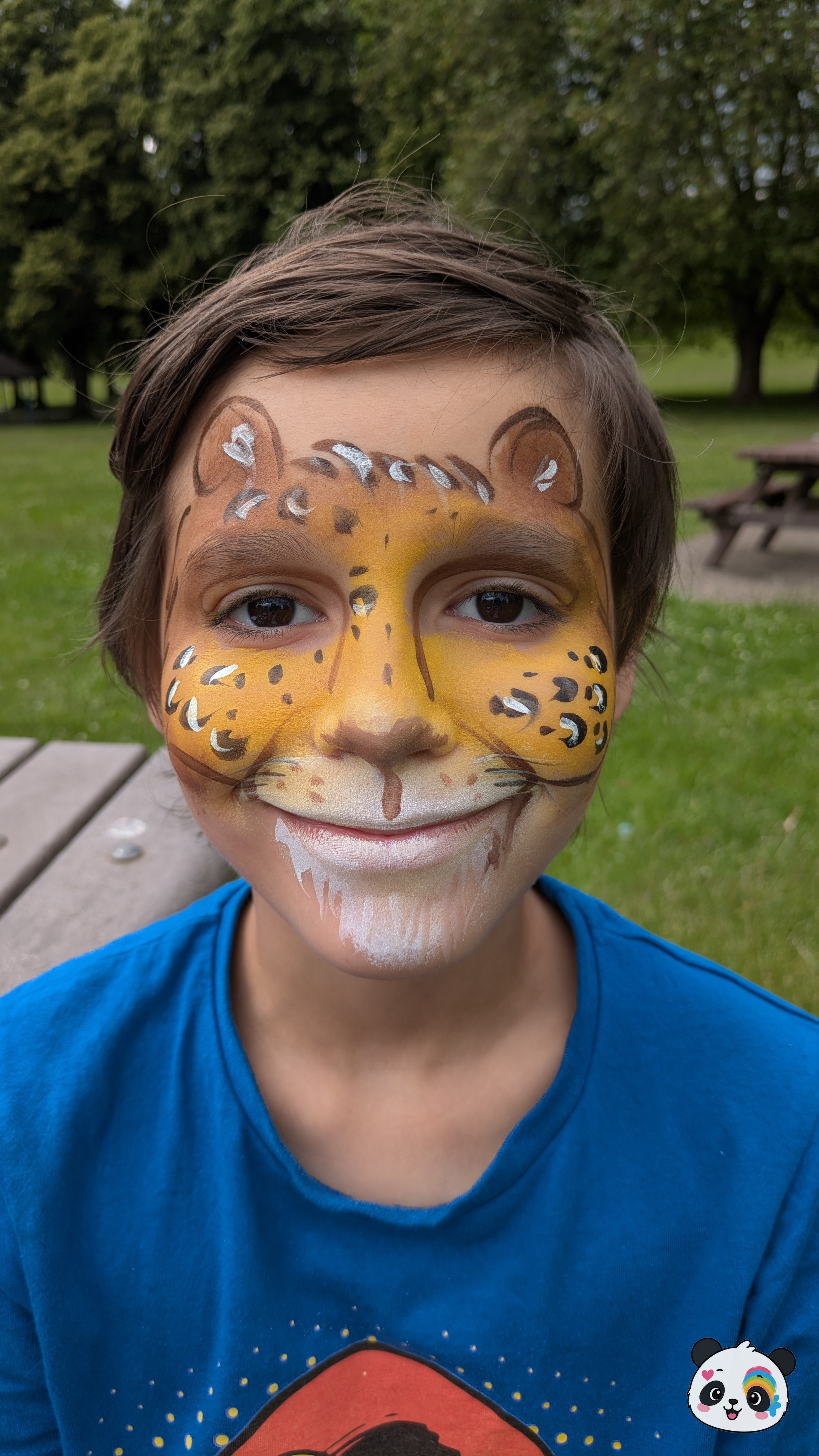Yellow and brown leopard face paint with black spots and white highlights covering the forehead, nose, and cheeks.