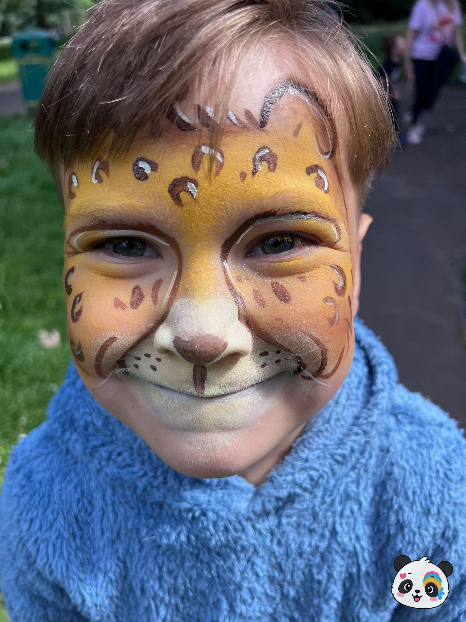 Yellow and brown leopard face paint with spots and whiskers covering the forehead, cheeks, and nose.