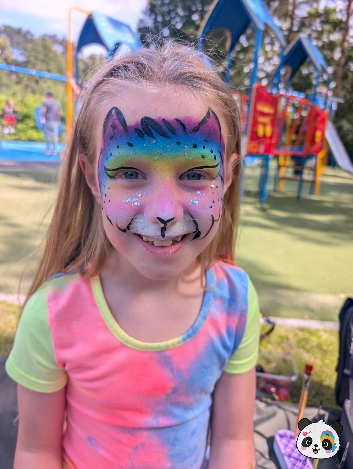 Rainbow gradient cat face paint with black line work, glitter accents, and a white muzzle on the full face.