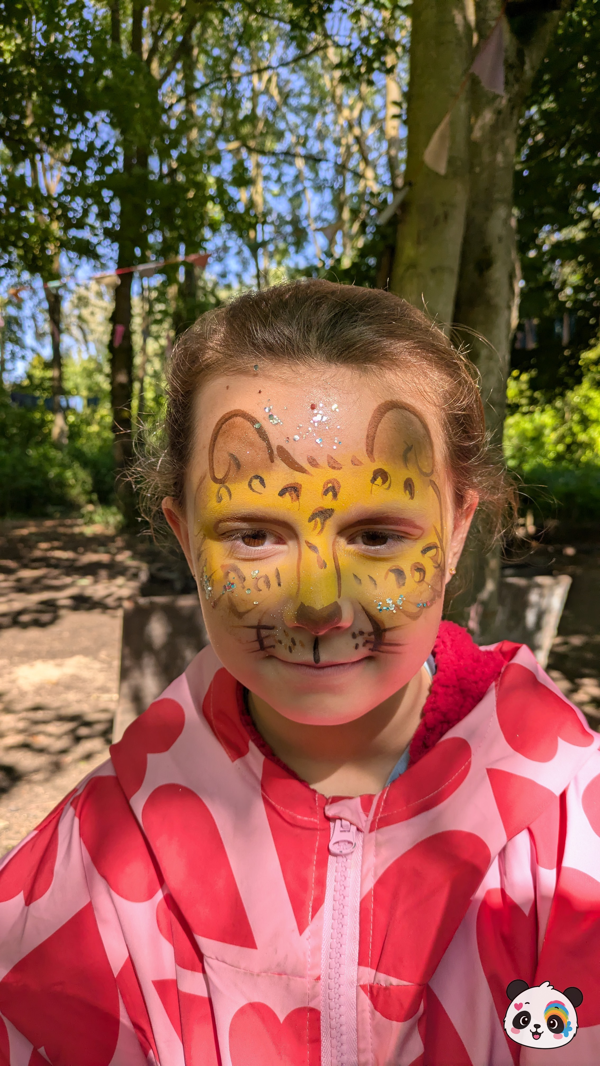 Yellow and brown leopard face paint with black spots, whiskers, and glitter accents across the forehead and cheeks.