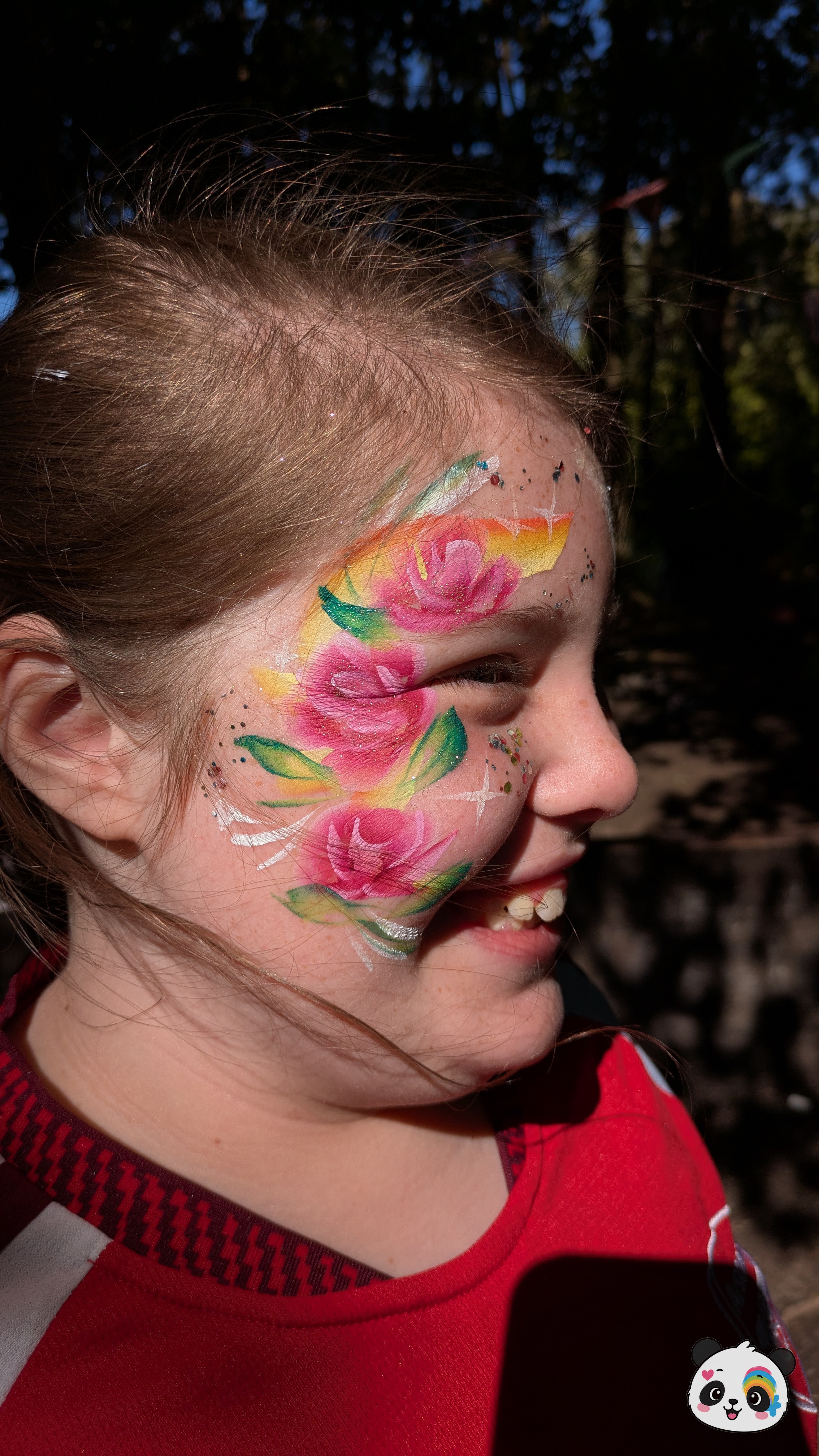 Pink roses with green leaves and yellow accents painted on the side of the face and temple with glitter details.