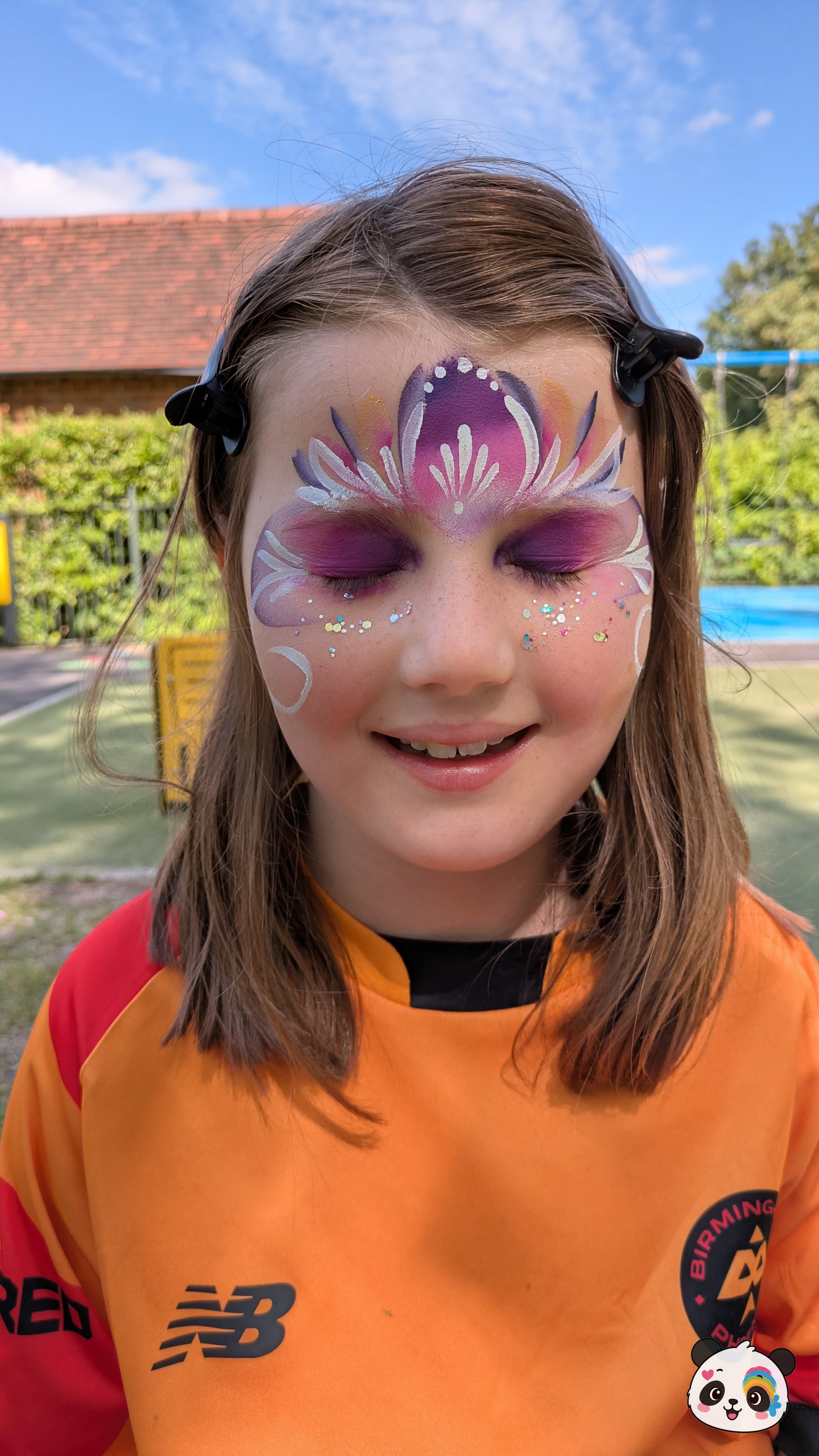 Purple, pink, and white floral crown face paint design across the forehead and eyelids with glitter accents.