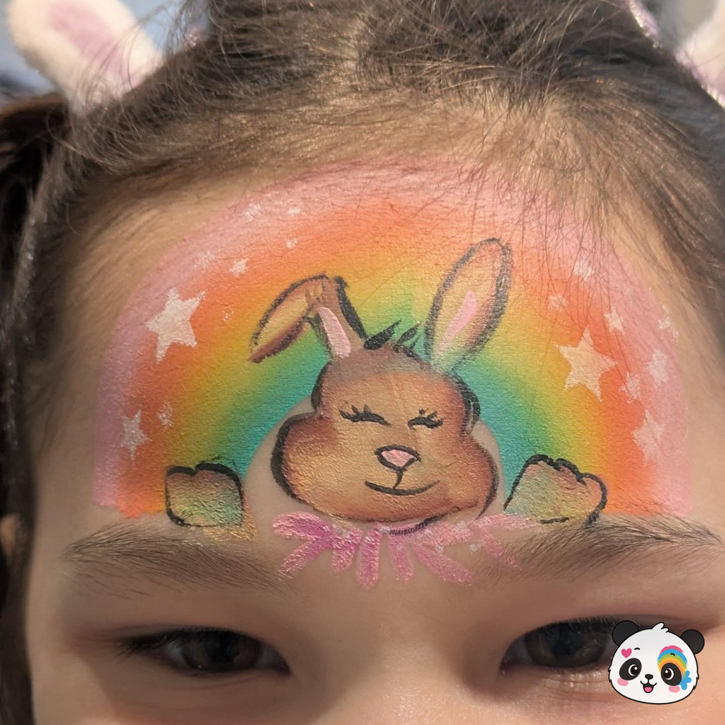 Cute bunny face paint on a rainbow background across a child's forehead