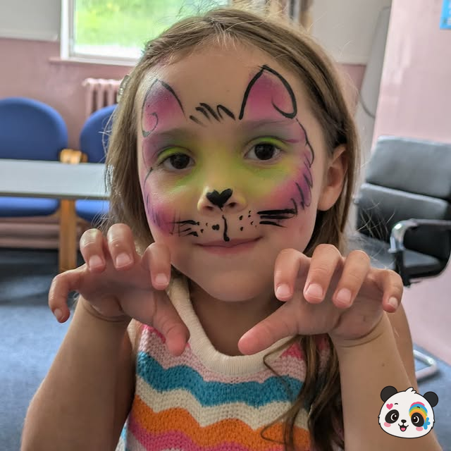 Pink and green cat face paint with whiskers on a smiling child