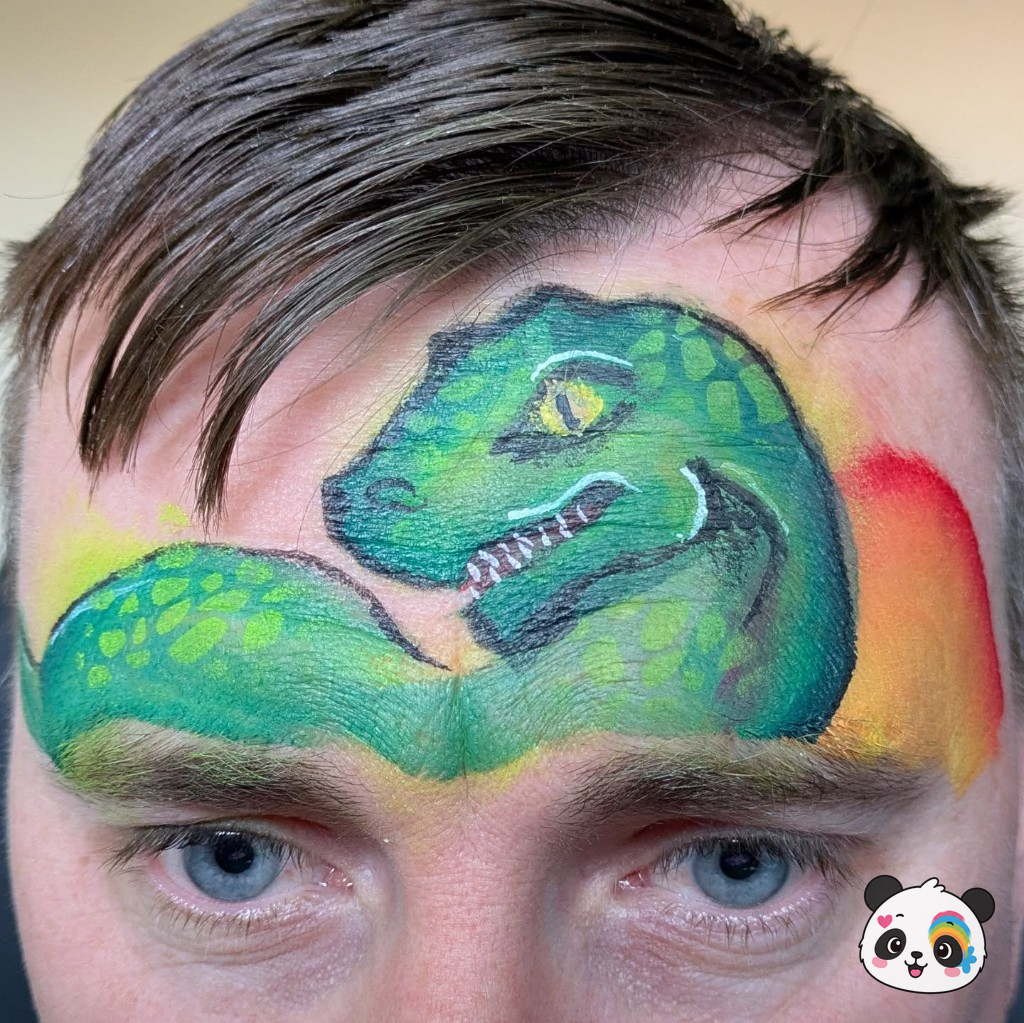 Green dinosaur face paint across a child's forehead with sunset background
