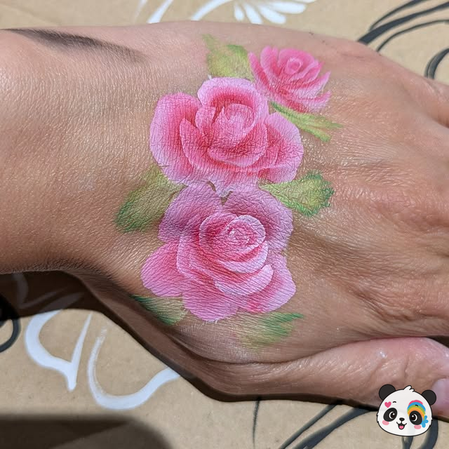 Three pink roses with green leaves painted on the back of a hand